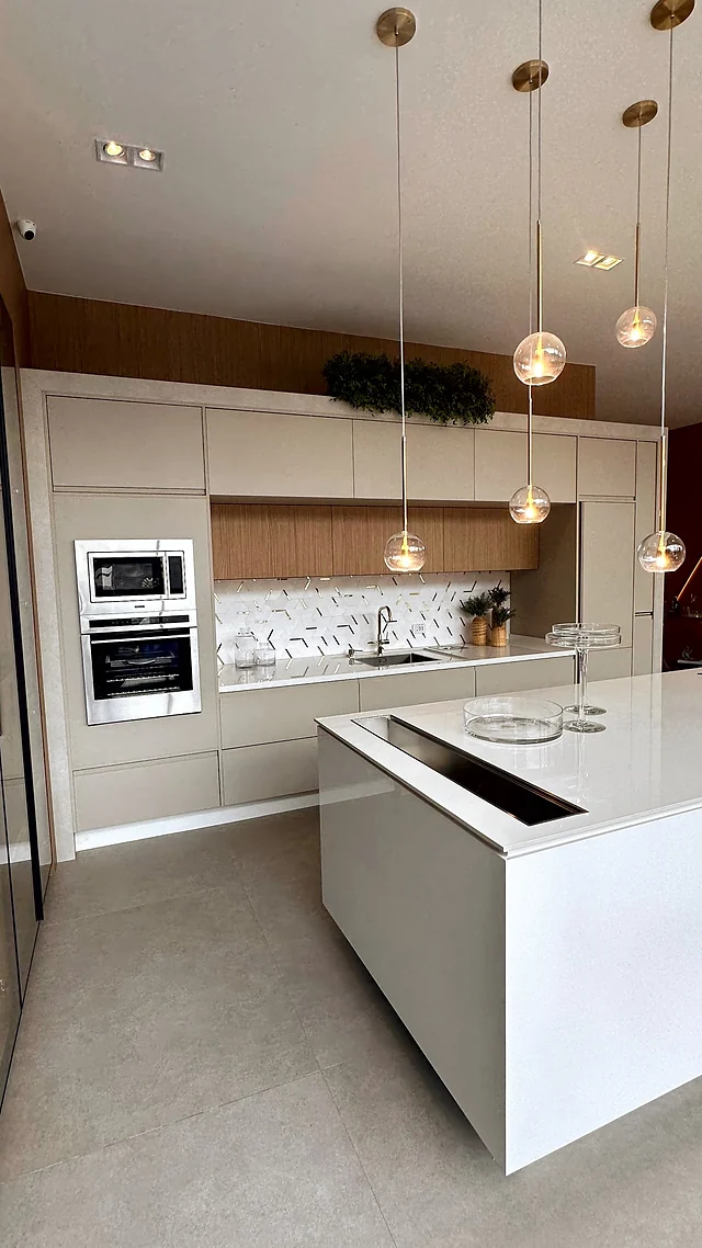 Cozinha planejada com ilha branca, cooktop, eletrodomésticos embutidos e pendentes acesos